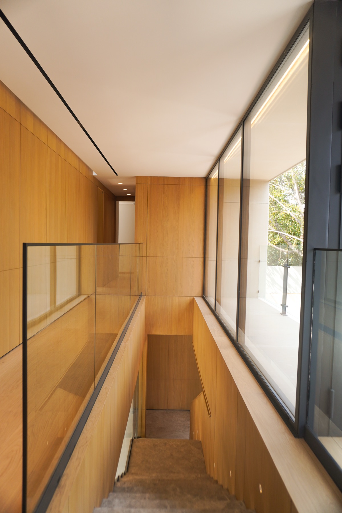 Pasillo de la planta alta con barandal de cristal y paneles de madera